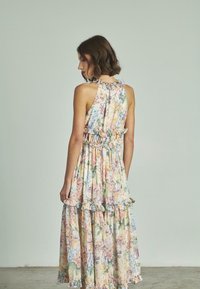 Abito maxi floreale in cotone leggero con colori pastello, rifiniture arricciate, strati a balze e lacci regolabili sul colletto.