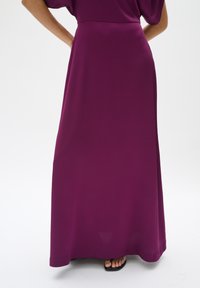 Robe maxi violette avec un tissu texturé, un design décontracté et une taille sans couture. Portée avec des sandales noires simples.