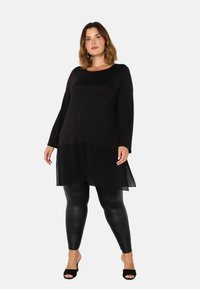 Musta tunika-mekko, jossa on pitkät hihat, läpikuultava alaosa, yhdistetty mustiin legginsseihin ja avointen varpaiden mustiin korkokenkiin. Silkkinen rakenne koko potra.