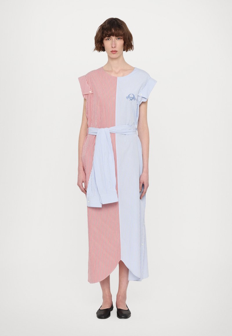 Robe rayée combinant des panneaux rouges et bleus, à manches courtes, taille ceinturée et ourlet asymétrique avec des boutons, fabriquée en tissu léger.