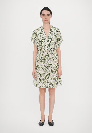 Korte bloemenjurk met een diepe V-hals, korte mouwen en een ceintuur op de taille. Heeft een witte achtergrond met groene bladeren en paarse bloemen.