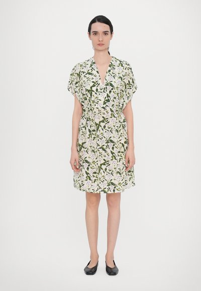 Robe fleurie courte avec un décolleté en V profond, des manches courtes et une taille ceinturée. Présente un fond blanc avec des feuilles vertes et des fleurs violettes.