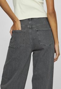 Vysokým pasem, šedé džíny z denimu s dvěma zadními kapsami, s mírně vybledlou texturou a klasickým prošitím podél švů.