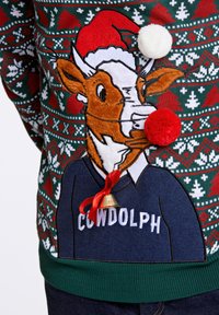 Sweter dziergany z wzorem krowy w czapce Mikołaja, z pomponami i dzwonkiem, w świątecznych kolorach zielonym, czerwonym i białym z wzorami.