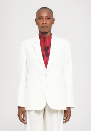 Witte blazer met een getailleerde pasvorm, twee knopen en gekleurde revers. Gecombineerd met een levendige rode bloemen sjaal, waardoor er een contrast in kleuren ontstaat.