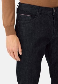 Temno modri jeans s ožjim krojem, ki imajo subtilno teksturo, zadnji žep z rožnatim šivom in klasično zapiralo na gumb.
