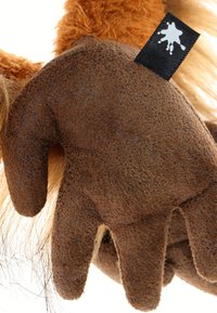 Gros plan sur une main en peluche marron texturée avec quatre doigts et une étiquette noire portant un logo en éclaboussure de peinture blanche.