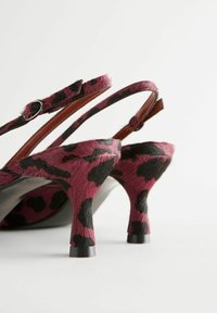 Pink and black leopard print high-heeled sandals with a textured finish, featuring a strap with a buckle and a curvy heel design.