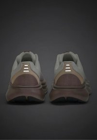 Para szarych i brązowych butów sportowych widziana od tyłu, z wyściełanymi kołnierzami wokół kostki i trzema odblaskowymi paskami na każdym pięcie.