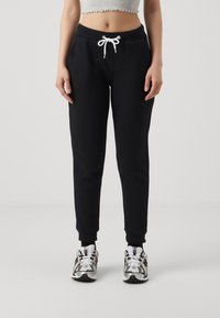 Black sweatpants with a drawstring waist, ribbed cuffs, and a soft texture, paired with white and silver athletic shoes.