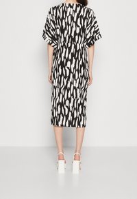 Vestido de estampado en blanco y negro con mangas cortas y sueltas, corte hasta la rodilla y cintura ceñida. Se lleva con sandalias de tacón grueso y blanco.