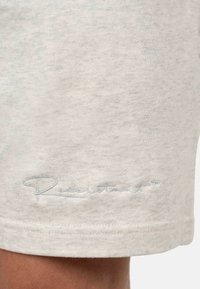 Shorts in cotone grigio chiaro con una texture morbida, orlo cucito e un logo ricamato sottile in un colore a contrasto vicino al bordo inferiore.