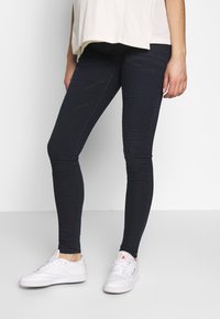 Jeans skinny azul escuro feitos de denim, com uma textura suave e um corte justo. Combinados com ténis brancos de desporto.