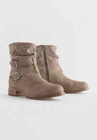 Bottines en cuir marron avec un tige repliée, deux boucles réglables, fermeture éclair latérale et un talon en bois empilé. Surfaces lisses et texturées.