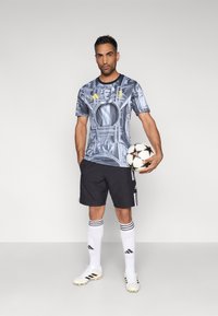 Μπλούζα ποδοσφαίρου με κοντά μανίκια και γραφικό σχέδιο σε μάρμαρο σε μπλε και γκρι, σετ με μαύρο σορτς, λευκές κάλτσες και ποδοσφαιρικά παπούτσια.