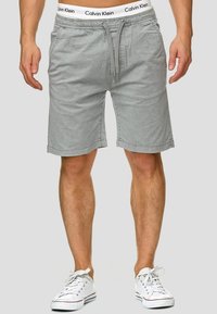 Shorts en coton gris avec taille à cordon, poches avant et ceinture logo Calvin Klein ; associés à des baskets blanches.