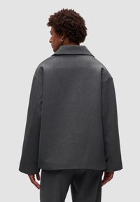 Zielonoszary, oversize, wełniany płaszcz z szerokim kołnierzem, opadającymi ramionami i mankietami. Gładka faktura z minimalnymi detalami.