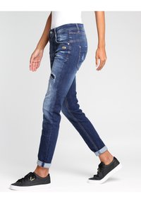 Slim-fit mörkblå denimjeans med slitagete detaljer, uppvikta ben och kontrasterande sömmar. Bärs med svarta sneakers.