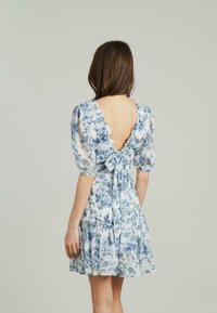 Abito a fantasia floreale in azzurro chiaro e bianco, con maniche a sbuffo, design senza schiena, orli arricciati e dettaglio a fiocco in vita.