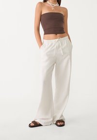 Bílé široké kalhoty s elastickým pasem a šňůrkou, spárované s přiléhavým hnědým topem bez ramínek a hnědými sandály. Hladká textura.