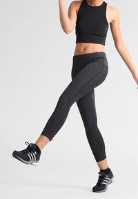 Top atletico nero corto e leggings grigi con accenti in rete. I leggings hanno una vestibilità aderente e materiale elasticizzato. Scarpe da ginnastica nere.