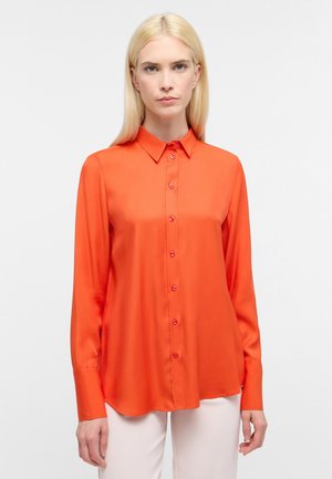 Camicia a maniche lunghe di un vivace arancione, con colletto a punta e sei bottoni davanti. Tessuto liscio, orlo leggermente curvo.