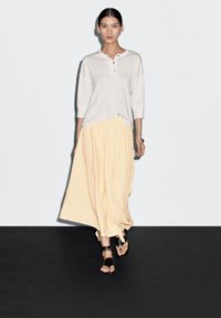 Jasnoszara bluzka z trzema ćwierć rękawami i guziczkami henley, zestawiona z zwiewną żółtą spódnicą i czarnymi sandałami na ramiączkach. Prosty design, miękki materiał.