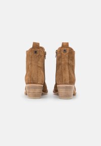 Braune Wildleder-Stiefeletten mit strukturiertem Finish, seitlichem Reißverschluss und gestapeltem Holzabsatz, versehen mit einem kleinen Akzentknopf nahe der Oberseite.