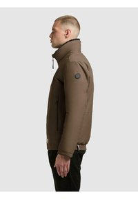 Brązowa ocieplana kurtka z wysokim kołnierzem, bocznymi kieszeniami na zamki oraz okrągłą czarną naszywką z logo na lewym rękawie. Gładka faktura.