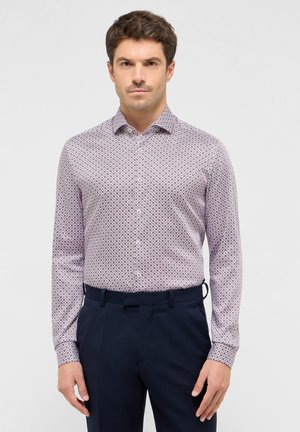 Witte shirt met een klein rood en blauw geometrisch patroon, met knoopsluiting en lange mouwen, gecombineerd met donkerblauwe broek.
