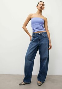 Top sin mangas de color púrpura claro y jeans de tiro alto de pierna ancha en color azul. Los jeans tienen bolsillos y cierre de botón, combinados con bailarinas de estampado de serpiente.