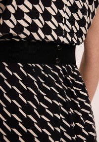 Czarna sukienka z białym abstractowym wzorem, z teksturowanym czarnym pasem w talii z zatrzaskami. Zbliżenie na tkaninę i detale wzoru.