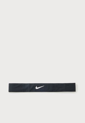 Черна лента за глава на Nike с бяло лого Nike swoosh, центрирано върху обикновен светлосив фон.