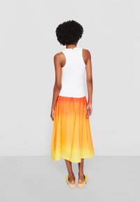 Weißes ärmelloses Oberteil kombiniert mit einem Rock in Orange-Gelb-Verlauf, der ein fließendes Design und eine bequeme Passform aufweist.