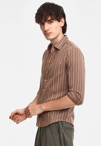 Camicia a righe marroni e bianche con una vestibilità comoda e maniche arrotolate, realizzata in un tessuto leggero. Presenta un orlo curvo.