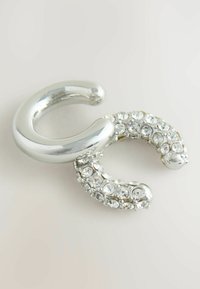 Sølvfarvet broche i en snoet design, der har en glat, skinnende overflade og en sektion udsmykket med klare rhinsten.