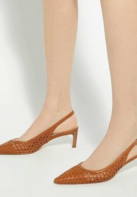 Brown cut-out slingback heels with a pointed toe, slender heel, and textured leather. Features an adjustable strap and open sides.