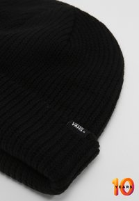 Cappello di lana nera a maglia con texture a coste e risvolto. Presenta un piccolo etichetta bianca "VANS" sul lato.