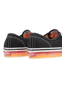 Chaussures en toile noires avec des coutures blanches, profil bas, dotées de semelles en caoutchouc dégradées orange et rouge avec le logo "mongoose".