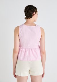Top senza maniche di un rosa chiaro con strisce bianche verticali, scollatura arrotondata e vita a peplum arricciato; abbinato a pantaloni corti di cotone bianchi.