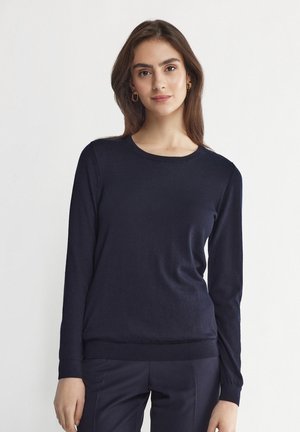 Mörkblå långärmad tröja i mjukt stickat tyg med rund halsringning och åtsittande nederdel. Har en slät yta och en minimalistisk design.