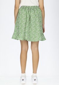 Gonna floreale verde con motivi di fiori bianchi, vita elastica, lunghezza al ginocchio, orlo svasato, abbinata a sneaker bianche e calzini.