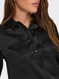 Schwarzes Satin-Hemd mit Knopfleiste und Kragen, das über eine glatte Textur und einen dezenten Glanz verfügt. Sechs schwarze Knöpfe zieren die vordere Knopfleiste.