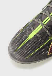Scarpa da calcio con una tomaia nera a trama, con accenti verde lime e rosa e un design a profilo basso. I lacci sono grigi.