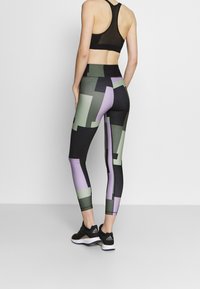 Czarny stanik sportowy z detalu z siateczki, zestawiony z legginsami o wysokim stanie z geometrycznym wzorem w zielonym i fioletowym na czarnym tle.