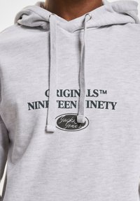 Hellgrauer Hoodie mit Kängurutasche, Kapuze mit Kordelzug und bedrucktem Text in dunkelgrün: "ORIGINALS NINETYNINETY" und "Jack & Jones."