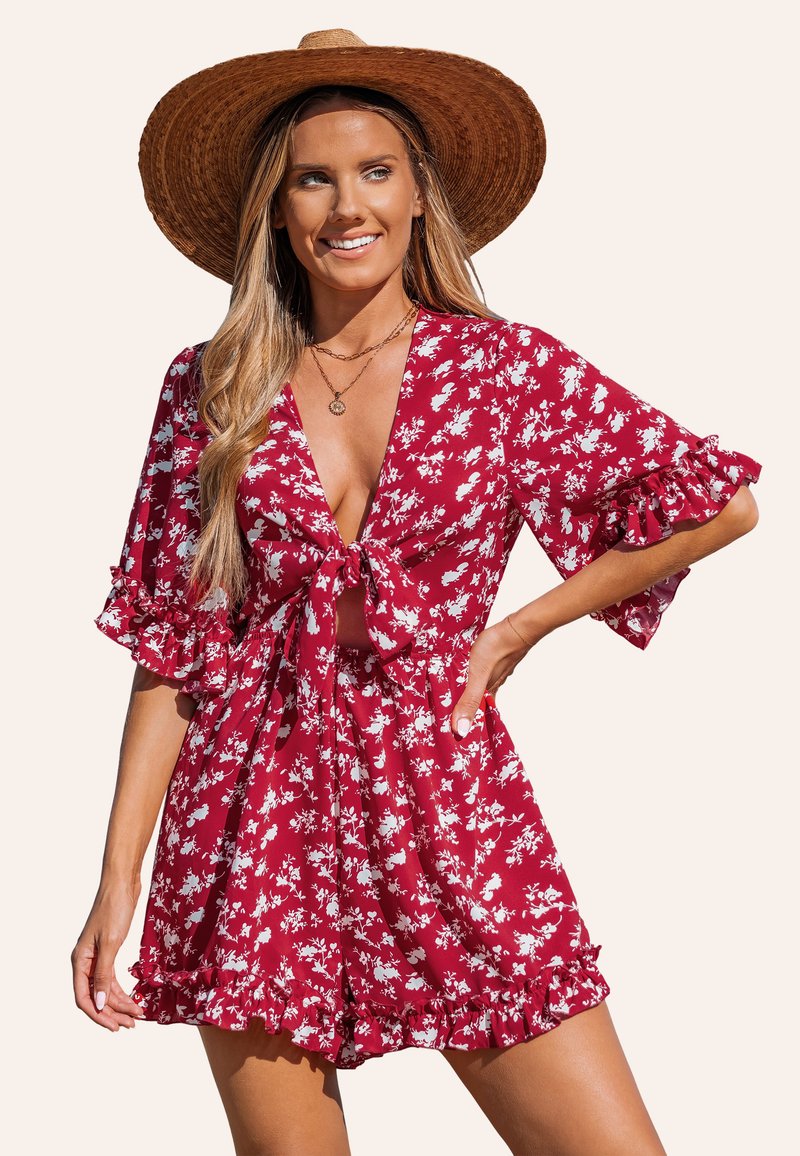 Tuta a fiori rossi con motivi bianchi, scollatura a V, apertura frontale con fiocco e maniche a volant. Tessuto leggero con vestibilità comoda e vita arricciata.