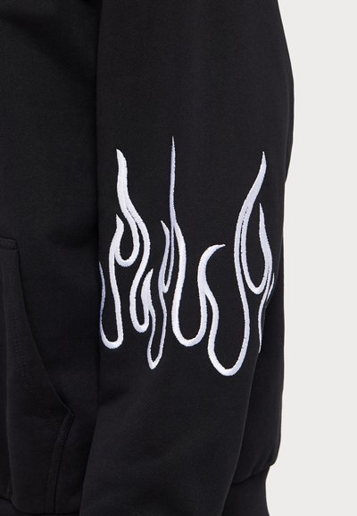 Sudadera negra con diseño de llamas bordado en blanco en la manga izquierda. Fabricada en un tejido texturizado y cuenta con un bolsillo frontal.