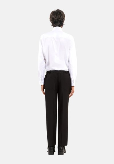 Witte lange mouwen shirt met verticale strepen, gecombineerd met zwarte broek met elastische tailleband en twee achterzakken.