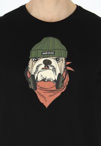 Musta t-paita, jossa on grafiikka bulldogista, joka käyttää vihreää pipoa ja kuulokkeita, ja sen alla on oranssi bandanakuosi.
